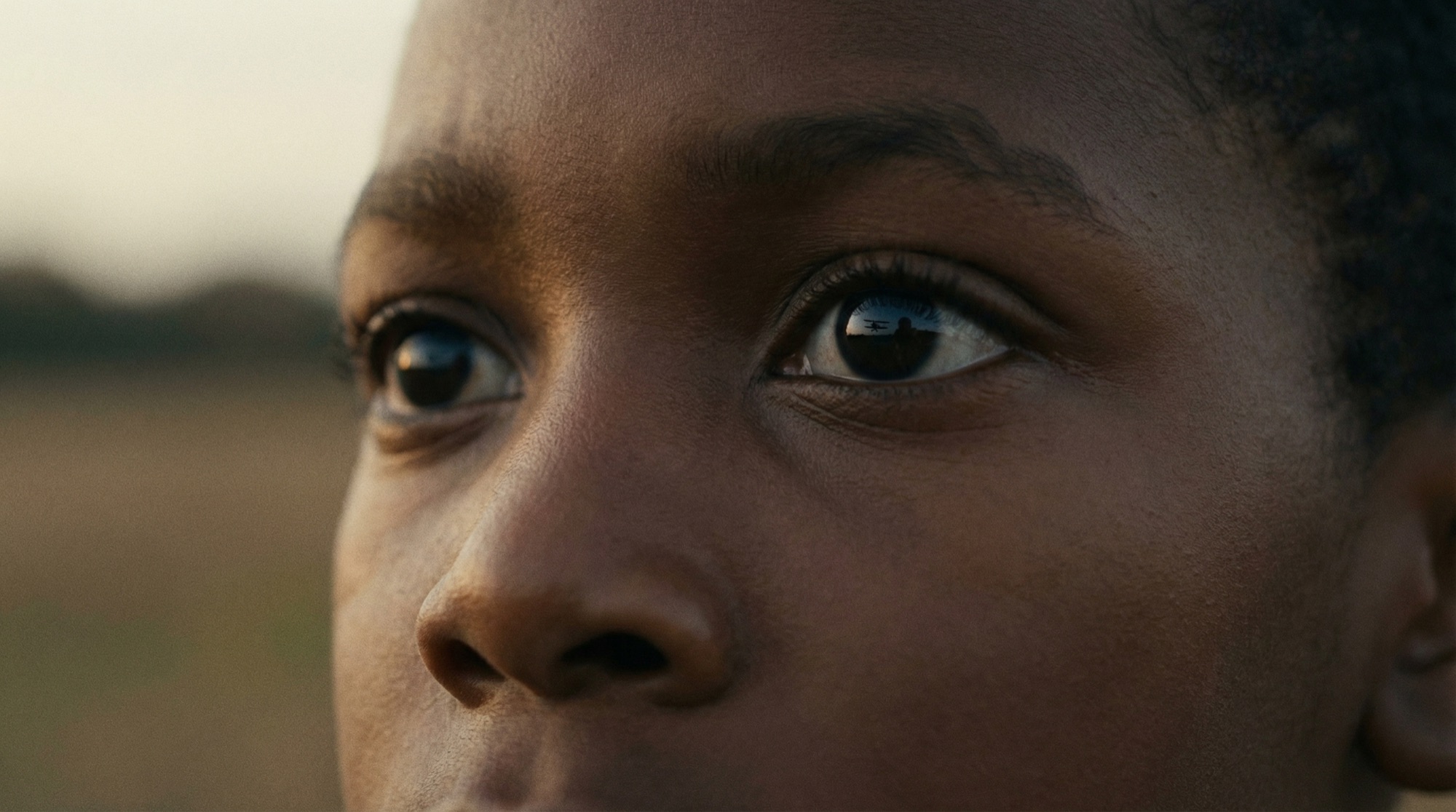 A close view of a young boy's eyes, a distant aircraft reflected in them.